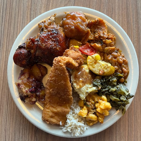 A plate from Georgia Comfort Kitchen with fried fish, chicken, rice, mac and cheese, collard greens, and baked beans.