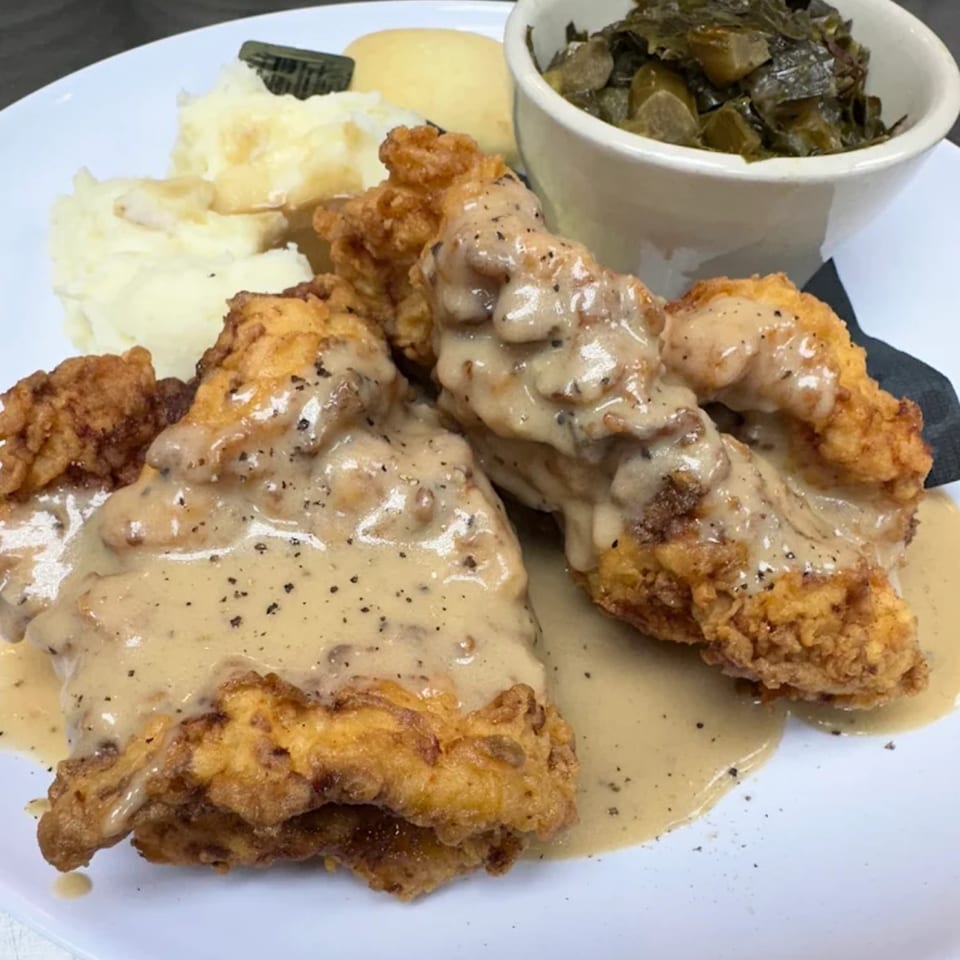 Fried chicken with gravy, mashed potatoes, a biscuit, and collard greens on a white plate.