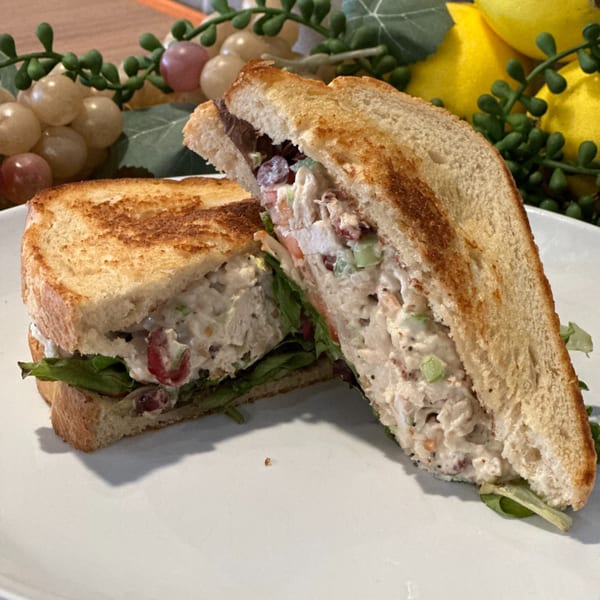 Toasted chicken salad sandwich with lettuce and tomato on a white plate, with decorative grapes and lemons.